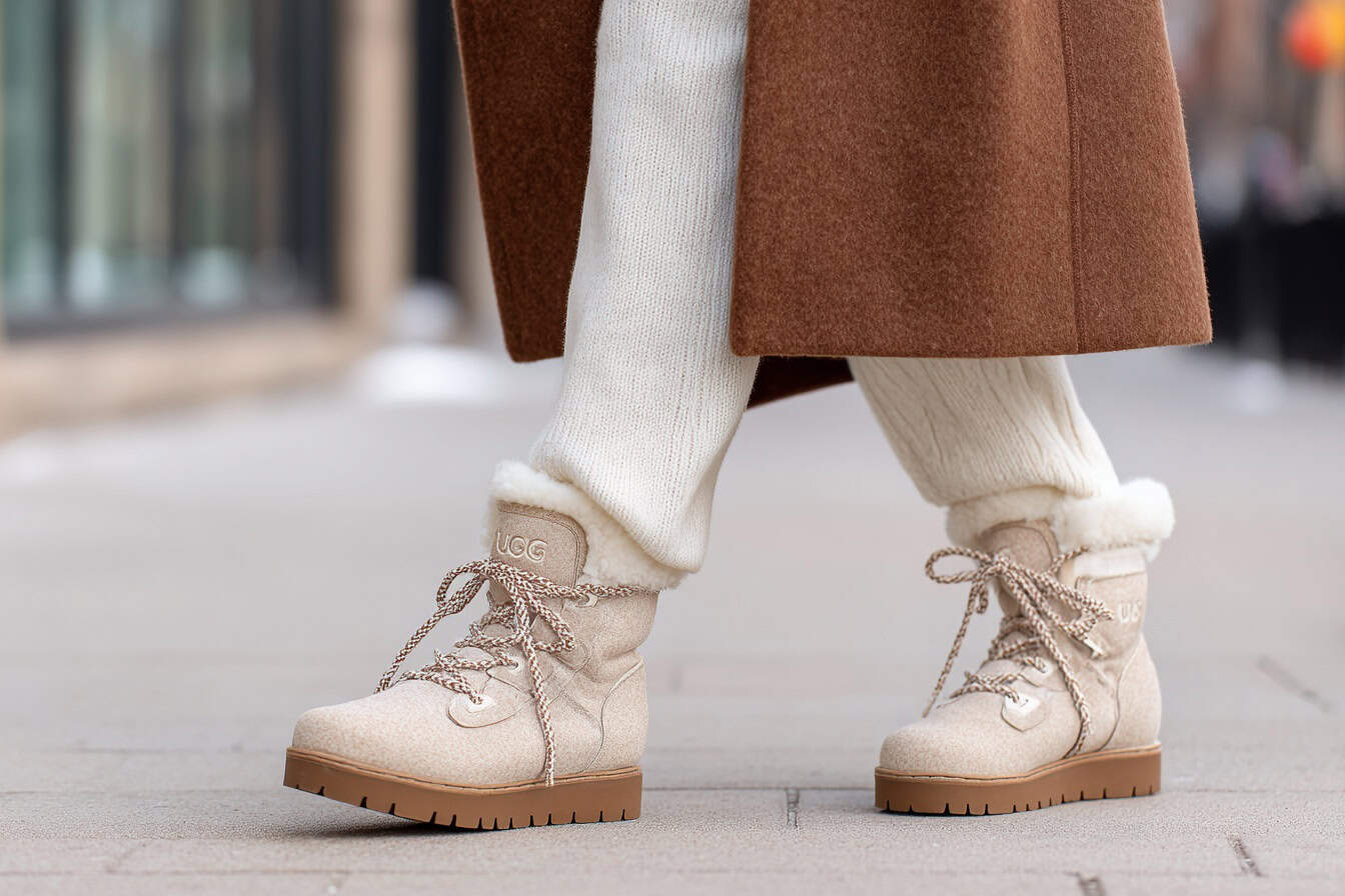 Beige Ugg boots paired with white knit trousers and a brown winter coat.